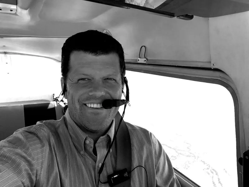 Austin grinning in the cockpit, wearing a headset, in black and white